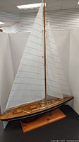 Full view of the wooden model sailboat showing the sails and hull on the stand.