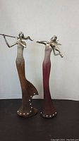 Full view of both musician statuettes side by side showing the flautist on the left and violinist on the right, illustrating the overall design and scale.
