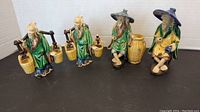 Four small vintage Asian ceramic figures on a dark surface with a white background, showing entire lot