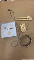 Multiple items arranged: gold brooches and ring in tray, carved ivory pieces, silver necklace and bracelet