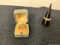 Two rings displayed together; one in a vintage box and one on a display cone.