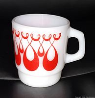 Side angle showing the red loops and teardrops design on the white milk glass mug