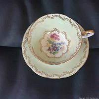 Top view of mint green teacup with central multicolored floral pattern and gold gilt detailing on rim and handle.