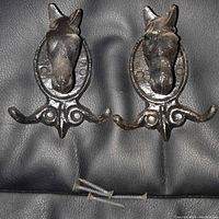 Front view of the pair of cast iron horse head coat hooks showing the horse head detail and triple prongs.