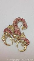 Close view of gold tone scorpion brooch showing pink rhinestones on body and claws with curved tail.