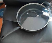 Top view of Starfrit frying pan with glass lid on black surface, showing pan's wide diameter and transparency of lid.