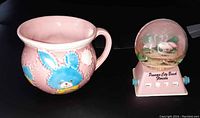 Photo showing both the pink ceramic baby nursery cup and the Florida souvenir flamingo snow globe day calendar together