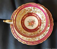 Top-down image showing the cup and saucer with red and gold floral pattern and rose floral center.