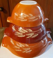 Three stacks of Pyrex Cinderella mixing bowls showing nesting and wheat pattern on orange background