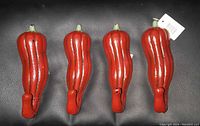 Four red chili pepper shaped metal hooks shown from the front on a black surface.
