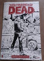 Front cover of The Walking Dead Artist's Proof Edition #1 comic book showing the artwork of a character facing away holding a gun with a broken window and destroyed car in the background, in black and white.