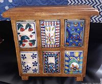 Front view of wooden chest showing six colorful hand-painted ceramic drawers with floral and geometric designs.