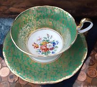 Top view of Aynsley cup and saucer showing green background with gold floral lace pattern, multicolor floral center in the cup
