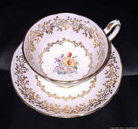 Top-down view of teacup inside saucer showing floral center, lilac border, and gold accents