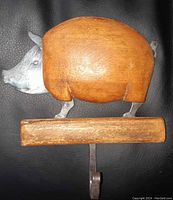 Front view of pig-shaped hook, showing wood body with metal head, legs, and tail, with attached metal hook under wooden base.