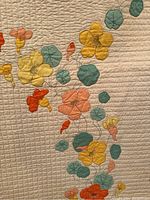 Close-up view of appliqué flowers in yellow, orange, pink with teal leaves on cream quilt fabric, showing quilted stitch details.