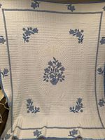 Full view of blue and white flower quilt showing central basket floral applique and border flower clusters.