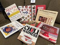 Photo showing 10 cookbooks on a sofa including Atkins for Life, My WW Program Cookbook, Montana Cookbook, and others.