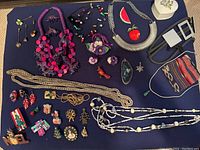Full view of assorted costume jewelry laid on dark fabric including necklaces, brooches, earrings, and jewelry pouches,