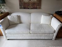 Front view of white upholstered loveseat sofa with two matching cushions placed at each side.