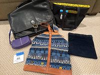Photo of all items including a black leather briefcase, black insulated lunch tote with yellow interior, small purple bag, patterned handbag, and a blue velvet bag on a carpeted floor.
