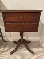 Front view of the vintage wood sewing table with two drawers and brass knobs, showing the pedestal base and legs.