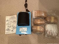 Lortone rock tumbler unit, tumbling barrel, instruction manual, and polishing compounds laid out on carpet.