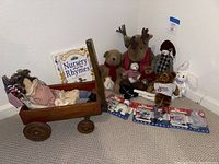 Wide view of the wooden wagon with two rag dolls inside and multiple large plush stuffed toys including Boyds Bear, moose, dog, plaid doll, and a white rabbit around it.