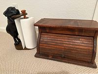 Photo showing the black dog paper towel holder and wood bread box together on carpet. The paper towel holder features a dog figure holding the paper towel roll horizontally.