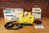 Full view of Karcher high pressure washer with box, manual, spray gun, hose, and extension lances arranged on wooden surface.
