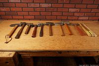 Front view of all hammers and mallets on a wood bench against brick wall