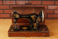 Front side angled view of the Singer sewing machine mounted on wooden base, showing decorative decals and hand wheel motor.