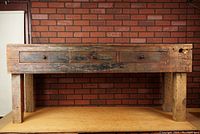 Front view showing entire bench with three drawers and four square legs against brick background