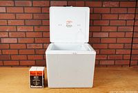 Vintage Koolatron Voyager portable cooler with its hinged lid open and Power Pack AC-11 converter placed next to it on a wooden surface against a brick wall backdrop.