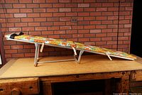 Side angled view of vintage floral exercise bench on folding aluminum frame showing full length and angled support bars.