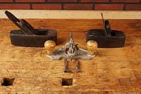 Overview of two dark wooden bench planes flanking a metal-bodied router plane on workbench