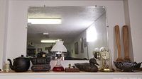 Overview of items on table with beveled wall mirror in background: oil lamp, mantle clock with glass dome, wooden duck decoy, kettle, decorative miniature stove, black pot.