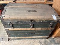 Front view of the antique wooden trunk showing metal latches, lock, and wood panels.