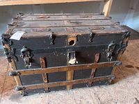 Front top view of antique trunk showing metal latches, leather strap, and lock area