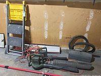 Photo showing folding step ladder, leaf blower/vacuum, extension cords, tire, and toolbox.