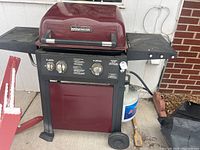 Full view of Brinkmann gas grill showing red lid, two side shelves, wheels and attached propane tank on right side