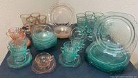 Full view of all pink and teal Indiana Glass depression glassware items arranged on a table including plates, goblets, cups, saucers, and shallow bowls.
