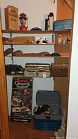 Shelving unit with Coleman lantern in box, Rapala cleaning station box, two tackle boxes open, and reels on shelf