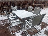 Full outdoor patio set showing rectangular glass top table and six matching metal rocking chairs with mesh seating, lightly covered in snow
