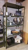 Full shelving unit with various kitchen items including large mixing bowl, glass jars, rolling pins, ice cream maker, and other metal kitchenware.