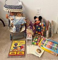 Photo showing full lot with vintage doll stroller holding two dolls, Mickey Mouse toy, Beatrix Potter books, small doll cradle, sidewalk chalk, children's books, and crayons.