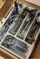 Drawer with organized stainless steel flatware and serving pieces in a plastic tray