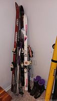 Photo showing all four pairs of skis, ski poles, and ski boots grouped together leaning against the wall.