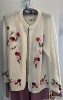 Full front view of the white knit sweater cardigan with floral embroidery, hanging on hanger.