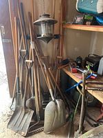Wide view showing yard tools leaning against a wall and workbench with a metal lantern hanging.